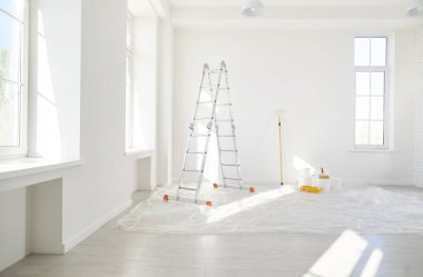 Basamaklı merdiven, yeni evdeki boş ışık odasında duran boya silindirli kovalar ya da yeni boyanmış beyaz duvarları olan bir daire. Evdeki yenileme işlemi. Ev onarımı ve taşınma günü konsepti.