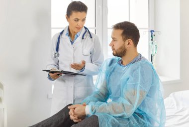 Beyaz üniformalı kadın doktor, hasta adama danışıyor ve şikayetlerini dinliyor, hastalığın nasıl tedavi edileceğini tartışıyor, bazı notlar ve reçeteleri panoya yazıyor.