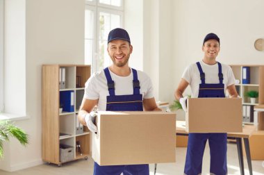 Üniformalı şirket çalışanları modern bir ofisten paket alıyorlar. Teslimat servisinden iki mutlu, neşeli, gülümseyen adam karton kutuları minibüslerine yüklemek için taşıyorlar.