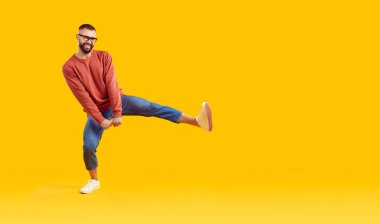 Modern kıyafetli komik bir genç fotokopi stüdyosunun arka planında dans ediyor. Turuncu kazaklı, mavi kotlu ve danseden mutlu adam sarı telif alanı arka planında izole edilmiş. Sıradan moda konsepti