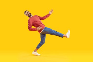 Neşeli, komik ve esprili genç adam turuncu arka planda büyük bir adım atıyor. Sıradan bir kazak, kot pantolon ve spor ayakkabı giyen yakışıklı adam kameraya bakarken adım atıyor. Tam uzunluk.