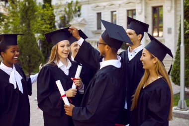 Genç adam havan tahtalarını düzeltiyor. Gülümseyen sarışın sınıf arkadaşına şapka takıyor. Mezuniyet şapkası ve tören cübbesi giymiş, diplomalarını ellerinde tutan çok uluslu grup öğrencilerinin portresi çok olumlu ve mutlu görünüyor..
