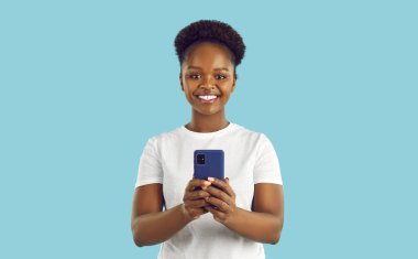 Beyaz tişörtlü, mutlu gülümseyen Afro-Amerikan kadın elinde akıllı bir telefonla turkuaz arka planda kameraya bakıyor. O bir fotoğraf çekiyor. Reklam pankartı