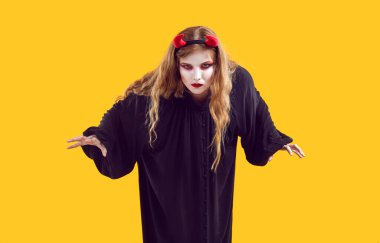 Sarı arka planda şeytani kılık değiştirmiş genç bir kız. Cadılar Bayramı kostümü giymiş bir kadın saldırmaya hazırlanıyor ve ciddi bir hipnotize edici yüz ifadesiyle kameraya bakıyor.