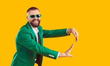 Aziz Patrick Günü partisinde eğlenen mutlu adam. Yeşil takım elbiseli komik sakallı adam ve parlak sarı arka planda yalnız dans eden güneş gözlüklü adam. Moda, parti, eğlence konsepti
