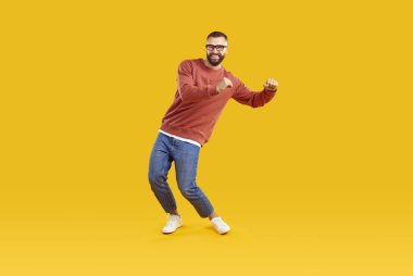 Sarı arka planda dans eden kırmızı kazaklı, kot pantolonlu ve gözlüklü esmer adamın uzun boylu portresi. Disko, dans, eğlence, reklam ve pazarlama konsepti.