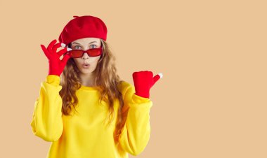 Cadılar Bayramı 'nda, sarı kazaklı, kırmızı şapkalı, eldivenli ve gözlüklü, bej arka planda gözlüklü, dalgalı, açık renk saçlı genç bir kadın. Sağ taraftaki kopyalama alanının başparmağı.