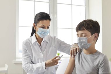 Kafkas doktor ve tıbbi maske takan bir kadın hastane içindeki bir hastanın omzuna şırıngayla tıbbi maske takan bir çocuğu aşıladı. Sağlık hizmeti kavramı.