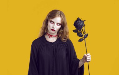 Elinde turuncu arka planda siyah gül olan gizemli, korkunç kadın portresi. Siyah elbiseli cadı kadın ve boynunda kanla Rose 'a korkunç bir bakışla bakıyor. Cadılar Bayramı konsepti.