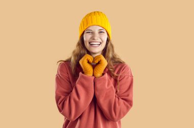 Mutlu, neşeli, sarışın, Avrupalı, modaya uygun koyu mercan kazaklı, rahat sarı şapkalı, yün eldivenli, neşeli yüzlü, gülen surat ifadeli, güz modası konsepti olan bir kadın.