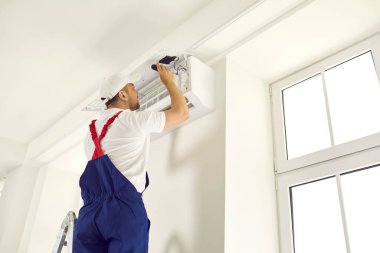 Genç teknisyen tornavida kullanır ve evdeki ya da ofisteki beyaz duvarda klima açar. Arka görüş, arkadan çekim. AC kurulum, bakım ve onarım hizmeti kavramı