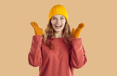 Mutlu, neşeli, neşeli, neşeli, gülümseyen, yakışıklı, koyu renk mercan eşofmanlı, sarı yün şapkalı ve kalın eldivenli Avrupalı, sarışın, beyaz bir kadının portresi.