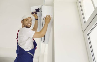 Teknisyen servisi. Müşteri dairesine yeni klima takan dost canlısı profesyonel erkek işçinin portresi. Gülümseyen adam tornavidayla klima donanımı kuruyor..