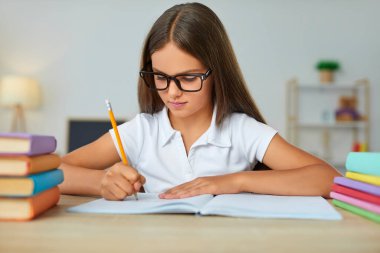 Okuldaki çocuk. Deftere yazan bir çocuk. Ödev yapan çocuk. Gözlüklü ciddi odaklı öğrenci sınıftaki masasında bir makale yazıyor. Okula, eğitime, öğrenme konseptine