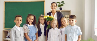 Mutlu okul zamanları. Birinci sınıf öğrencilerinin okulun ilk gününde bayan sınıf öğretmenleriyle portresi. Çiçek buketi olan bir kadın sınıfında genç öğrencilerinin arkasında duruyor. Pankart.