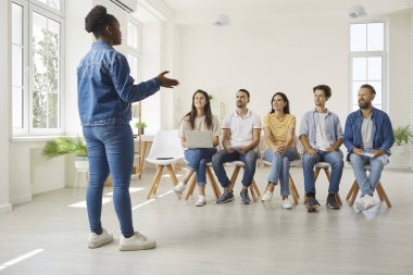 İşletme koçu, motivasyon konuşmacısı ve bir grup işçiyle iletişim uzmanı konuşuyor. Bir grup insan sırada oturup Afrikalı Amerikalı kadınların tecrübelerini ve hayatlarını paylaşmalarını dinliyorlar.