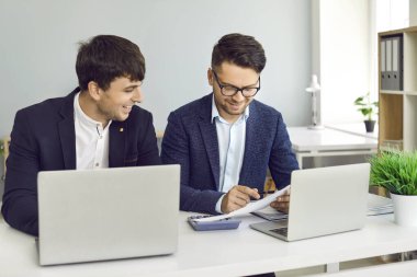 Gündelik kıyafet giyen bir grup iş adamı dizüstü bilgisayar kullanıyor, konuşuyor, iletişim kuruyor, planlama yapıyor, ofiste çalışıyor. Ofisteki iki iş arkadaşı masada oturup dizüstü bilgisayarda yazı yazıyorlar..