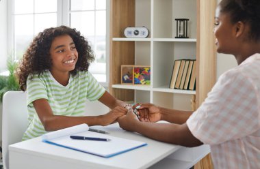 Çocuğun psikologla ya da okul danışmanıyla güvenilir bir ilişkisi var. Küçük mutlu çocuk, bir uzmanla masada oturuyor, ellerini tutuyor ve gülümsüyor. Psikolojik yardım, destek kavramı