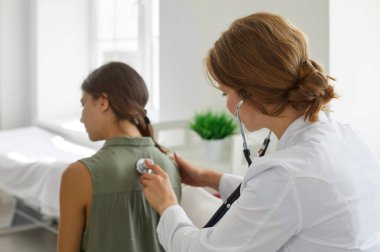 Steteskoplu bir doktor bir çocuk hastayı muayene ediyor. Beyaz önlüklü bir kadın doktor genç bir kızın akciğerlerini inceliyor. Sağlık, klinik, sağlık kontrolü konsepti