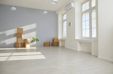 Yeni dairedeki boş oturma odasının zemininde içi boş karton kutular ve yeşil bir bitki duruyor. Taşınma, taşıma, teslimat, gayrimenkul veya ipotek konsepti.