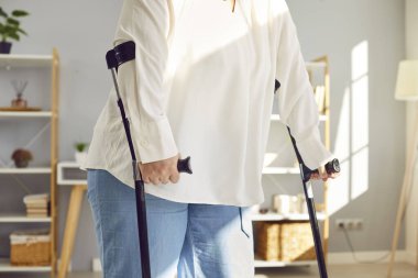 Yürümek için koltuk değneği kullanan şişman bir kadın yaralandı. Kesilmiş dolgun bir atış, artı koltuk değnekleriyle evde duran boyunda bir kadın. Tedavi ve obezite sorunları