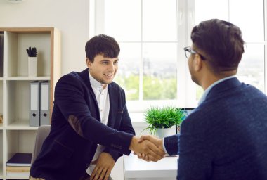İki kişi iyi bir iş anlaşması yapar ve el sıkışırlar. Ofis masasında oturup, birbirlerine bakıp el sıkışan genç adamlar..
