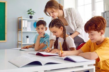 Beyaz çocuk kız ve erkek ilkokul öğrencileri not defterine not alan bayan öğretmenler görevlerini yerine getirirler. Ortaöğretim alırlar.