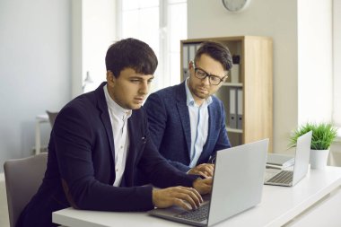 İki konsantre iş adamı ortak iş projesinde birlikte çalışıyor. Takım elbiseli ciddi gençler dizüstü bilgisayarlarla aynı masaya oturur ve iş kurma kavramını geliştirirler. İş konsepti.