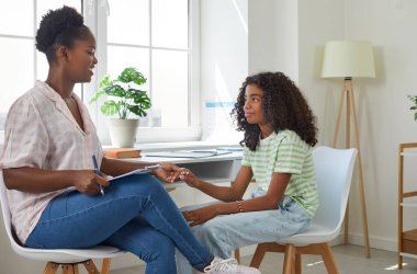 Gülümseyen Afro-Amerikan kadın psikolog terapi seansında genç kızın yanında el ele tutuşuyor. İletişim kurmak, terapi, psikoterapi, çocuk konsepti için psikolojik yardım.