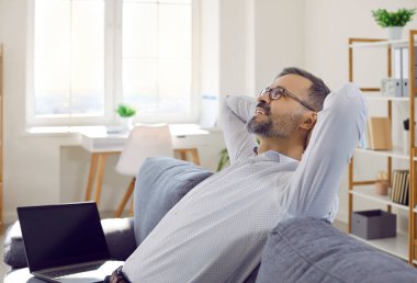 Rahatlama zamanı. İşinden memnun olan adam, ellerini başının arkasına koyarak boş zamanlarından zevk alır. Hayalperest suratlı bir iş adamı rahat bir koltukta dizüstü bilgisayarın yanında oturuyor..