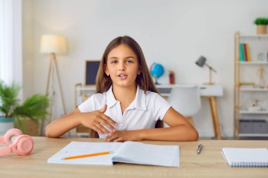 Online sınıfta bir ilkokul çocuğunun portresi. Video araması ile. Evdeki masasında oturmuş kameraya bakıyor ve ödevi hakkındaki soruları cevaplıyor.