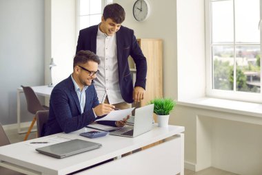 Ofiste gülümseyen mutlu iş adamları. Takım elbiseli iki genç işveren sevinçle konuşuyor ve tartışıyorlar, yeni projeleri ve girişimleri değerlendiriyorlar, şirketi analiz ediyorlar. Takım çalışması konsepti.