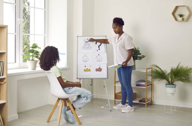 Afro-Amerikalı kadın psikolog, genç kızlara sosyal ilişkiler kurmak için ilan panosunda kart göstermeyi öğretiyor. Duygusal zekanın gelişimi, terapi, psikoterapi, psikolojik yardım.