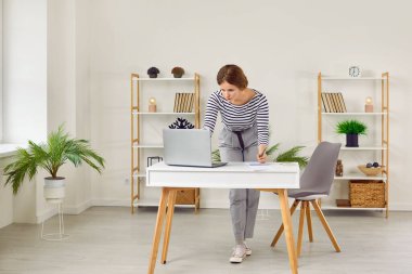 Ofiste dizüstü bilgisayarla çalışırken not defterine not alan yoğun genç bir kadın. Kadın iş yerinin yanında duruyor ve aceleyle internetten ya da e-postadan bilgi yazıyor..