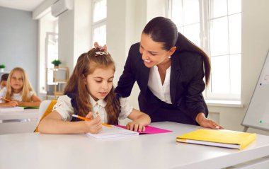 Eğitim, öğretim ve bilgi. Ders sırasında sınıfta öğretmenlik yapmak küçük kız öğrencinin okul ödevini tamamlamasına yardımcı olur. Küçük kız elinde not defteriyle masada oturuyor..