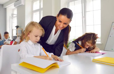 Öğretmen ilkokul çocuğuna görevinde yardım ediyor. Sınıfta çocukların yazı yazmasına yardım eden güler yüzlü bayan öğretmen. İlkokul eğitimi konsepti