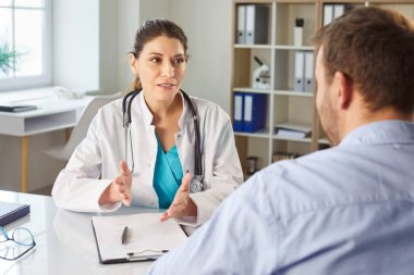 Muayene sırasında klinikteki masada oturan dost canlısı bayan doktorun tavsiyelerini dinleyen genç bir hastanın portresi. Sağlık ve Tıp Konsepti.