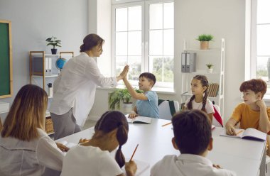 İyi iş çıkardın. İyi iş çıkardın. Çak bir beşlik. Mutlu okul öğretmeninin küçük çocuklarla iyi ilişkileri vardır, öğrencileri yeni bilgiler edinmeye teşvik eder ve daha iyi sonuçlar ve başarılar için motive eder.