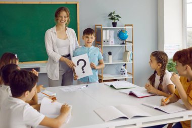 Okuldaki psikoloji. Küçük okul çocuğu ve okul psikoloğu grup dersi sırasında soru işaretini tutuyorlar. Pozitif kadın psikolog ilkokul öğrencileriyle grup terapisi yapıyor..