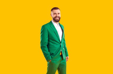 Yeşil takım elbiseli mutlu genç adamın stüdyo fotoğrafı. Sarı arka planda elini cebine sokup poz veren şık yeşil takım elbiseli yakışıklı erkek modelin portresi. Erkek moda konsepti