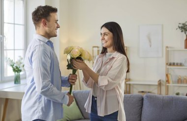 Kadınlara bir buket gül veren mutlu bir adam, özel bir durumla tebrik ediyor, sıcak ev içlerine karşı poz veriyor. Koca, karısına çiçekler sunar, romantik bir ilişki yaşar.
