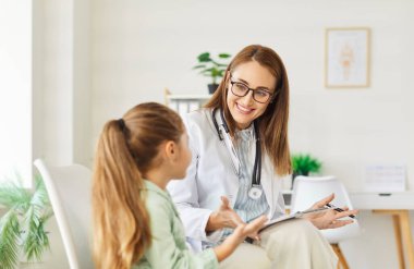 Dost canlısı bir pediyatrist doktorun portresi, klinikteki iş yerinde oturan ve tıbbi muayeneden sonra tavsiyelerde bulunan küçük kız hastasıyla konuşuyor..