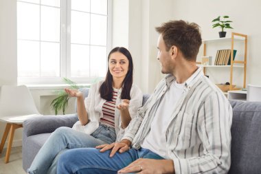 Parlak oturma odasındaki rahat koltukta oturan gülümseyen genç çift arkadaşça sohbet ediyorlar. Mutlu karı koca birlikte iyi vakit geçiriyorlar, evde olumlu duygular paylaşıyorlar..