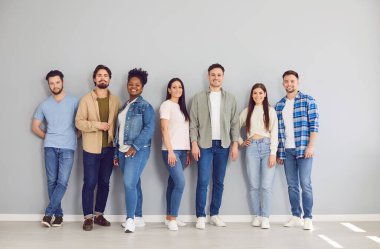 Kendine güveni tam bir grup genç arkadaşın portresi. Günlük giysiler içinde gri bir duvarda yan yana duran ve kameraya olumlu bakan öğrenciler veya meslektaşlar..