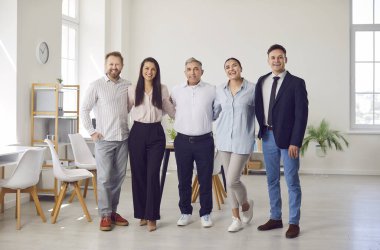 Modern bir ofiste birlikte duran profesyonel iş arkadaşlarının mutlu grup portresi. Çalışan olumlu insanlardan oluşan bir ekip, takım çalışmasını ve olumlu çalışma ortamını vurguladı.