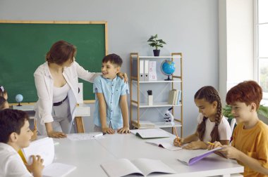 Dost canlısı gülümseme öğretmeni tahtada cevap veren küçük bir çocuğu zevkle dinler. İlkokul öğrencileri modern ve modern okullarda yaratıcı dersteler. Eğitim kavramı.