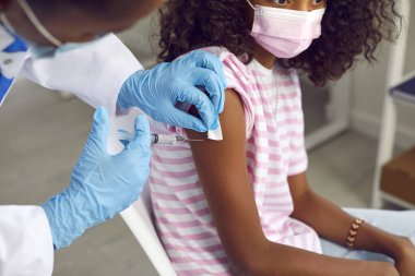 Afro-Amerikalı genç kız hastanede aile doktorundan grip aşısı oluyor. Doktorun eldiven temizleme yerindeki yakın çekimi. Bağışıklık, önleme ve hastalıkların tedavisi kavramı.