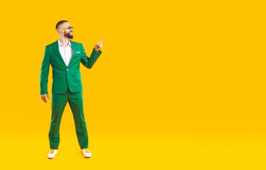 Şuna bir bak. Yeşil takım elbiseli mutlu genç adam stüdyoda duruyor, Aziz Patrick Günü 'nün reklamını yapıyor, sağa sola işaret ediyor ve sarı fotokopi arkaplanda bir şeyler gösteriyor.