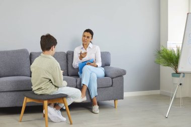 Profesyonel kadın psikolog, ofisinde terapi seansında bir çocuğa danışmanlık yapıyor. Çocuk psikoterapisti kanepeye oturmuş not defterine not alıyor. Terapi, psikolojik yardım, çocuk konseptine destek.