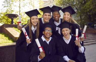 Yüksek eğitim almak. Akademik elbiseler ve diploma tomarları taşıyan mutlu mezunların toplu portresi. Çok ırklı erkek ve kadın üniversite mezunları fotoğraf çekimi için birlikte poz veriyorlar..